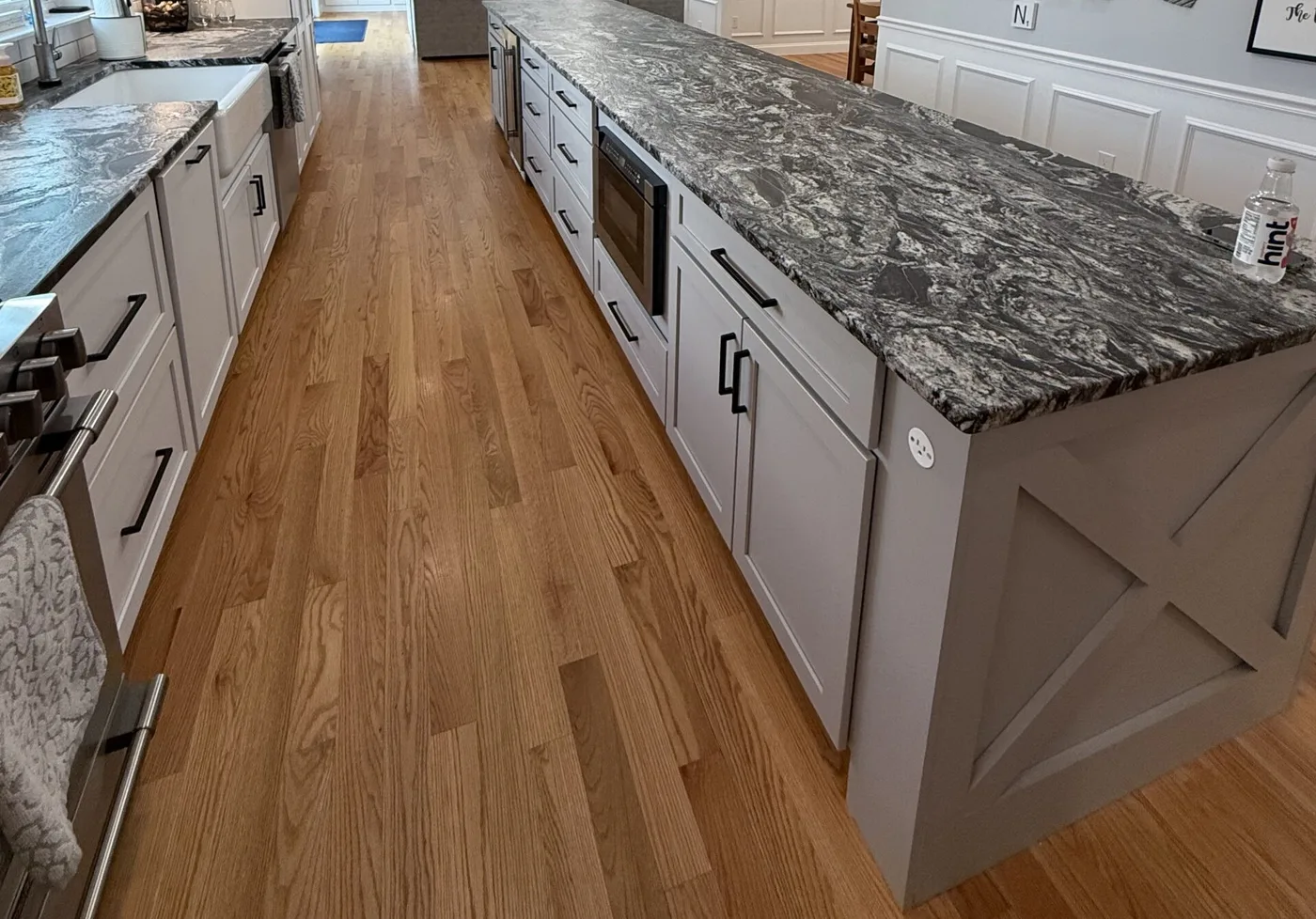 Long kitchen island with bold gray and white stone veining, white cabinetry, and wood flooring