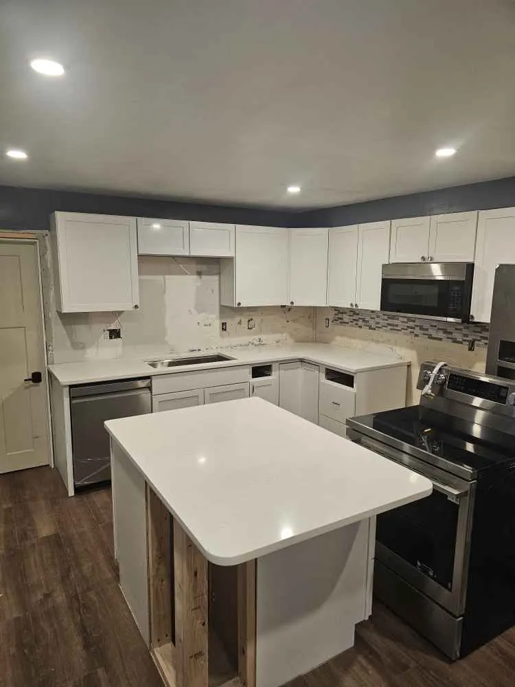 Compact kitchen island with rounded white countertop corners near a range and surrounding cabinets
