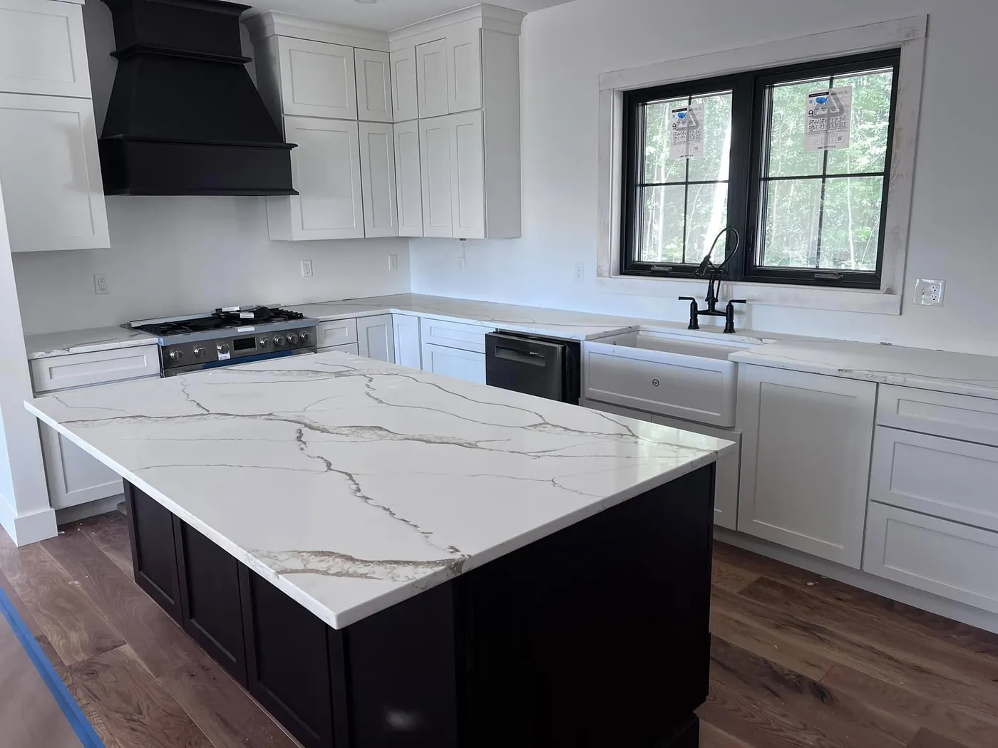 White kitchen with coordinated veined stone countertops on a black island and white perimeter cabinets