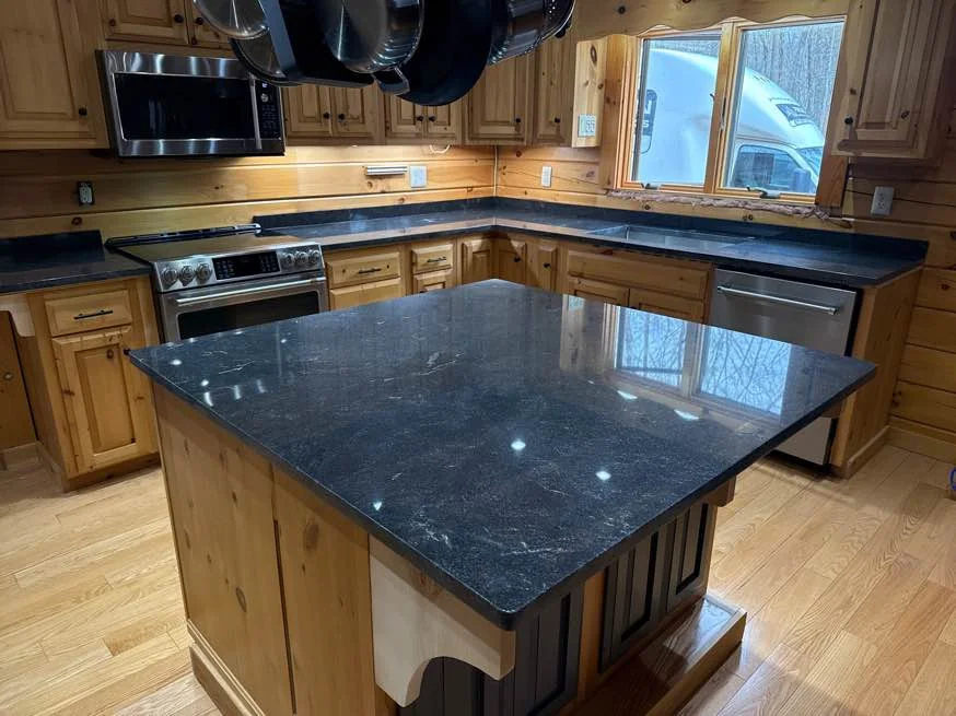 Polished Jet Mist granite kitchen island with a simple edge profile beside natural wood cabinets