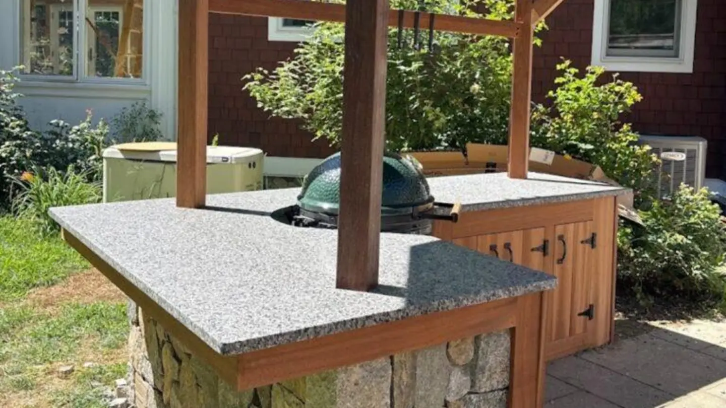 Outdoor kitchen with a granite countertop on a stone base in a New Hampshire backyard