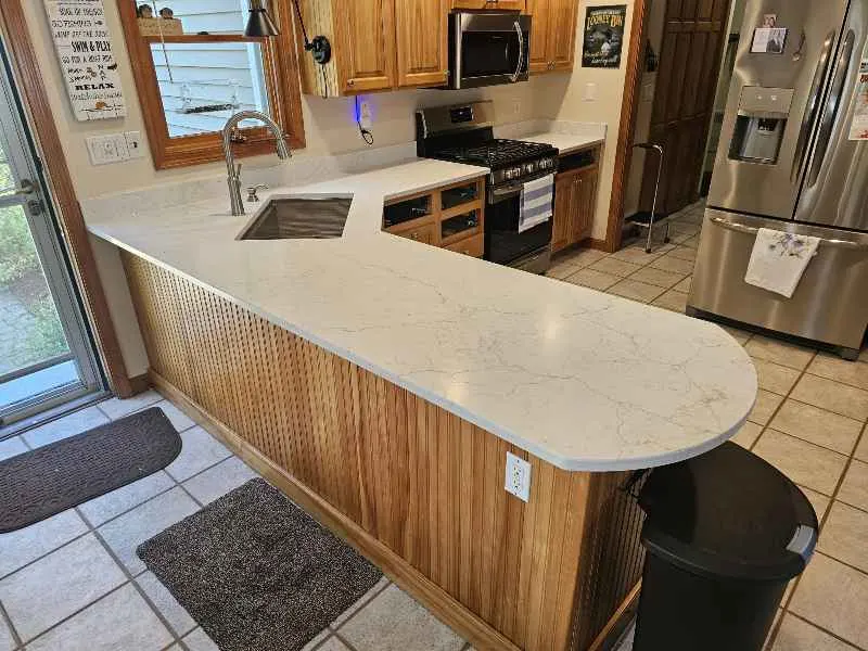White quartz kitchen peninsula with a rounded projecting end over a wood cabinet base