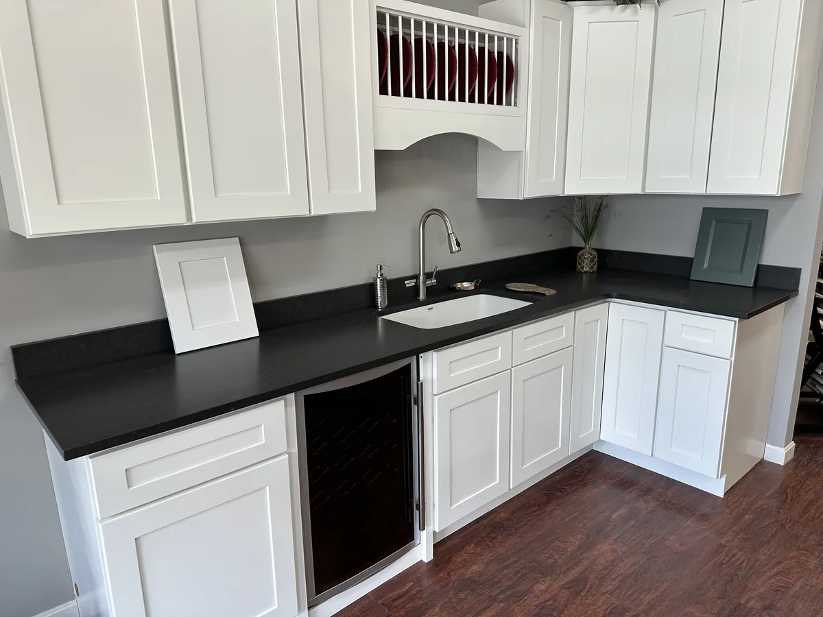 Full L-shaped soapstone countertop display at the Precision Granite Works showroom in Epsom NH — installed on white shaker cabinets with undermount sink and wine fridge