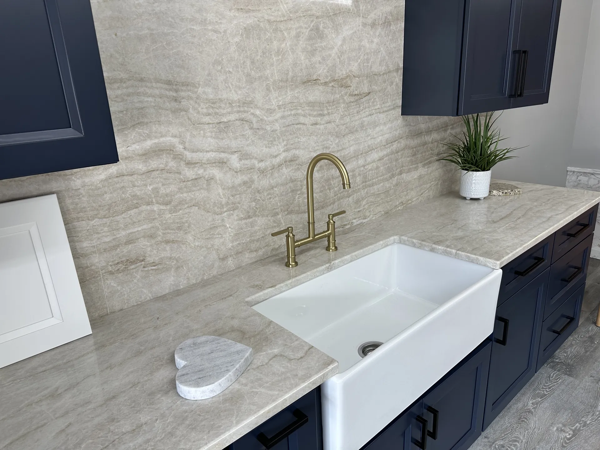 Premium quartzite countertop with farmhouse sink and brass bridge faucet on display inside the Precision Granite Works showroom in Epsom NH