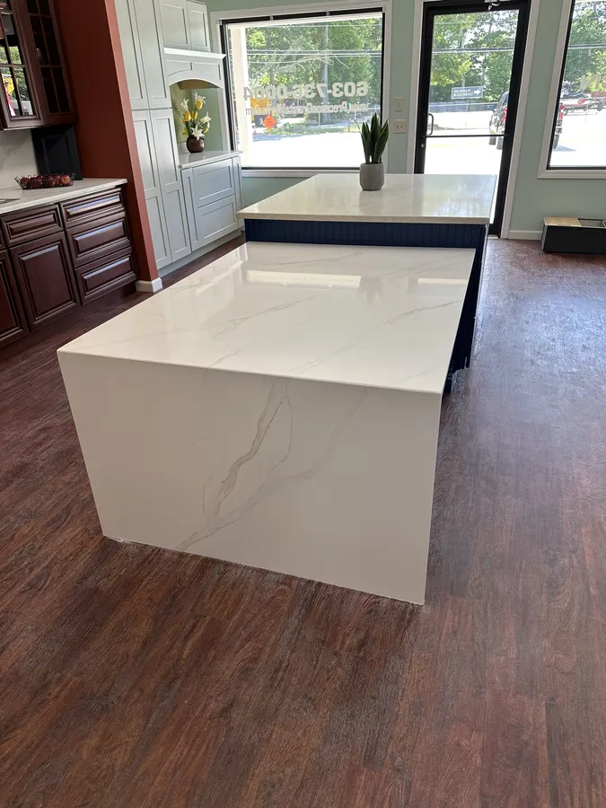 Single-end white quartz waterfall countertop display with an open seating side and navy island cabinetry