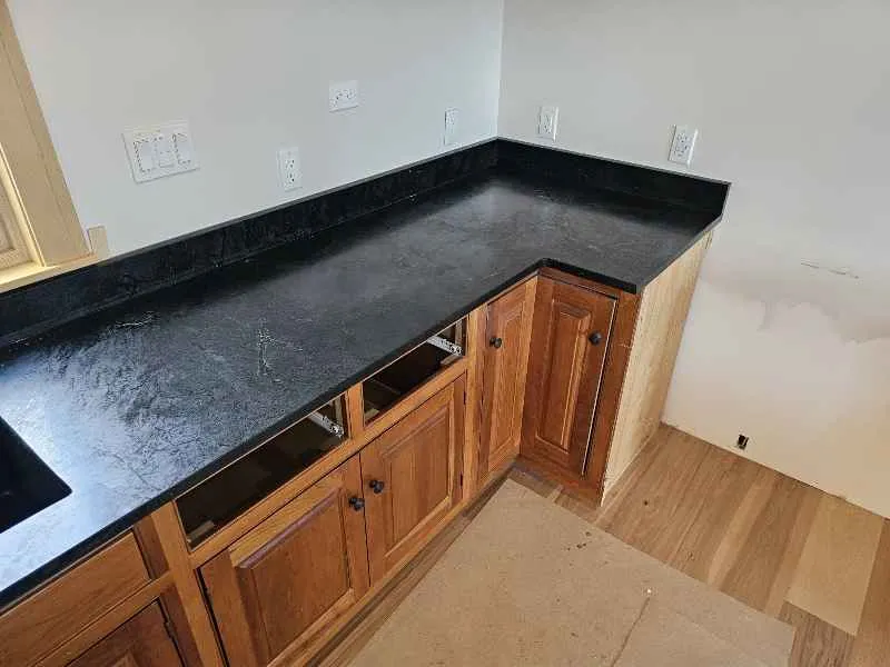 Soapstone countertop corner with matching stone backsplash and warm wood cabinetry