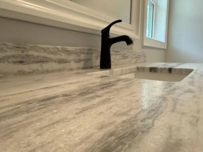 Close-up of a polished white stone countertop with gray veining and matching backsplash panel — laundry room installation by Precision Granite Works in New Hampshire