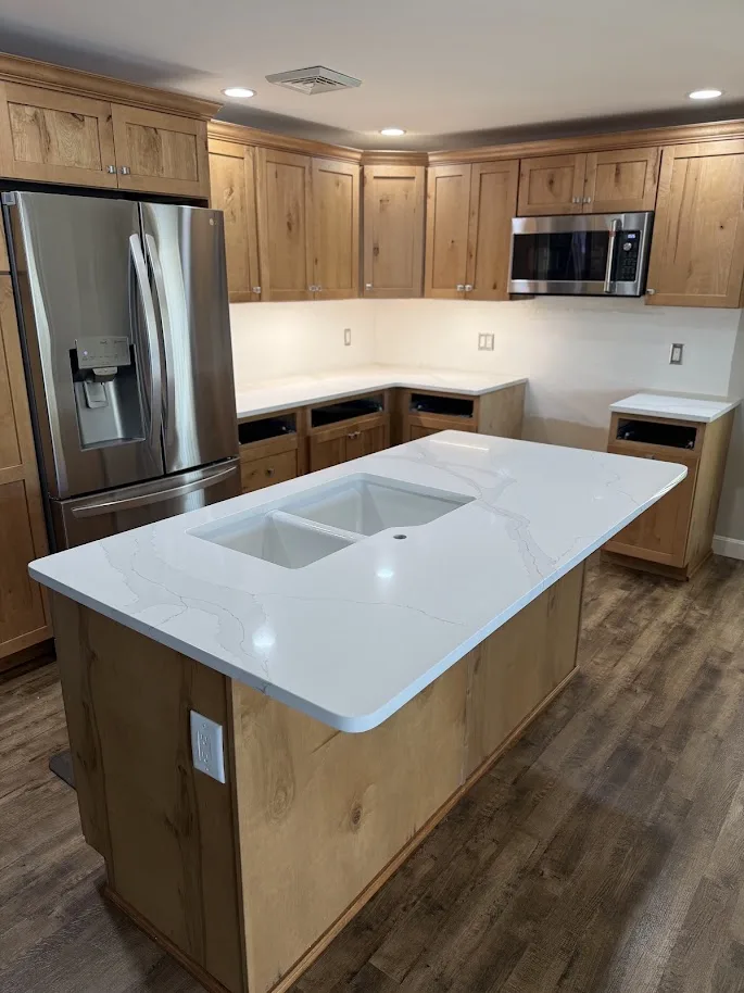 Subtle movement white quartz kitchen island with undermount sink and natural wood cabinets — Precision Granite Works NH