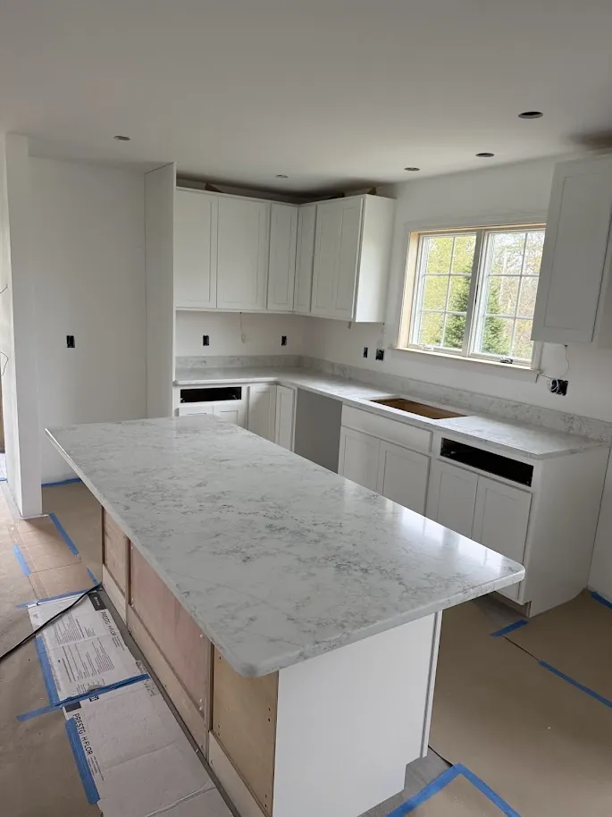 Light natural stone kitchen island and perimeter countertops with white cabinets in New Hampshire