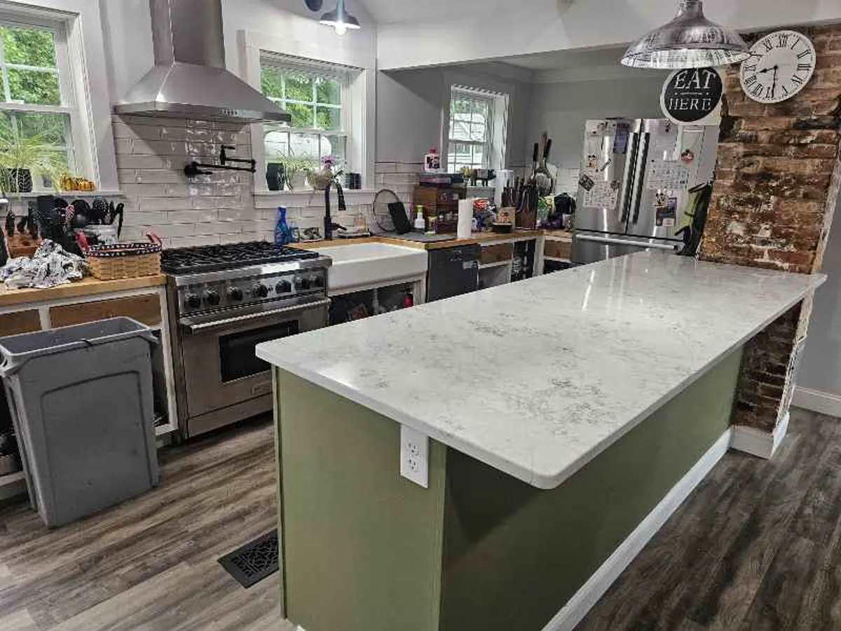 White quartzite kitchen island with soft movement paired with green painted island cabinet — installed by Precision Granite Works NH