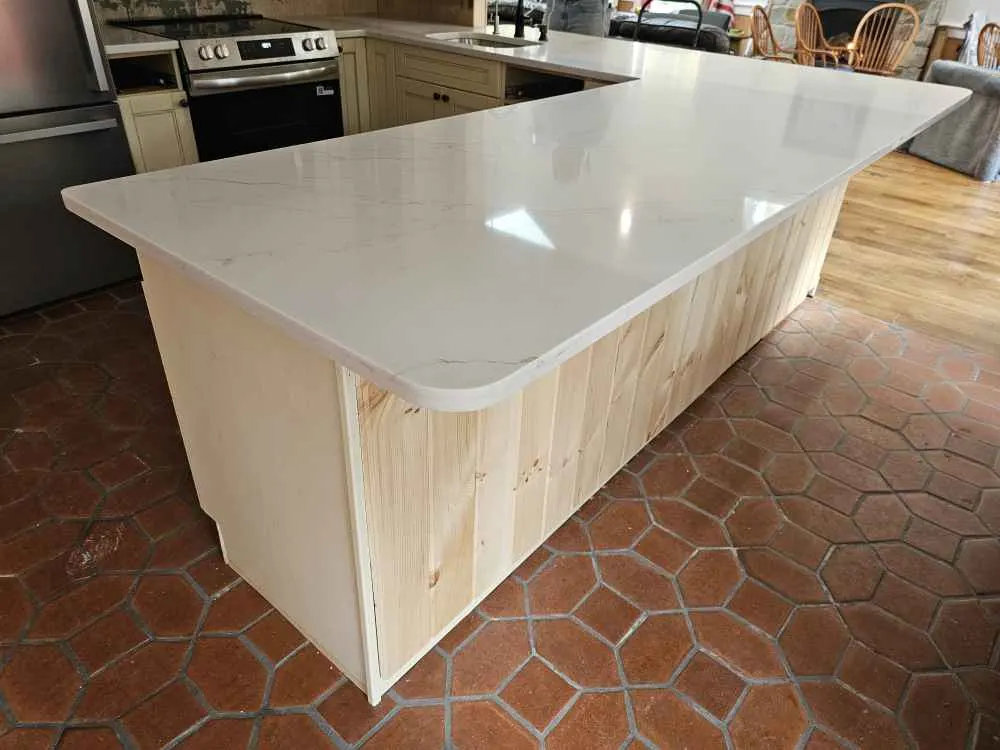 White kitchen island countertop with rounded corner projecting beyond a straight paneled cabinet base