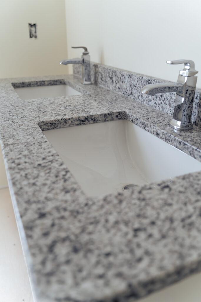 A white, grey, and black speckled granite bathroom sink countertop on white cabinets underneath.