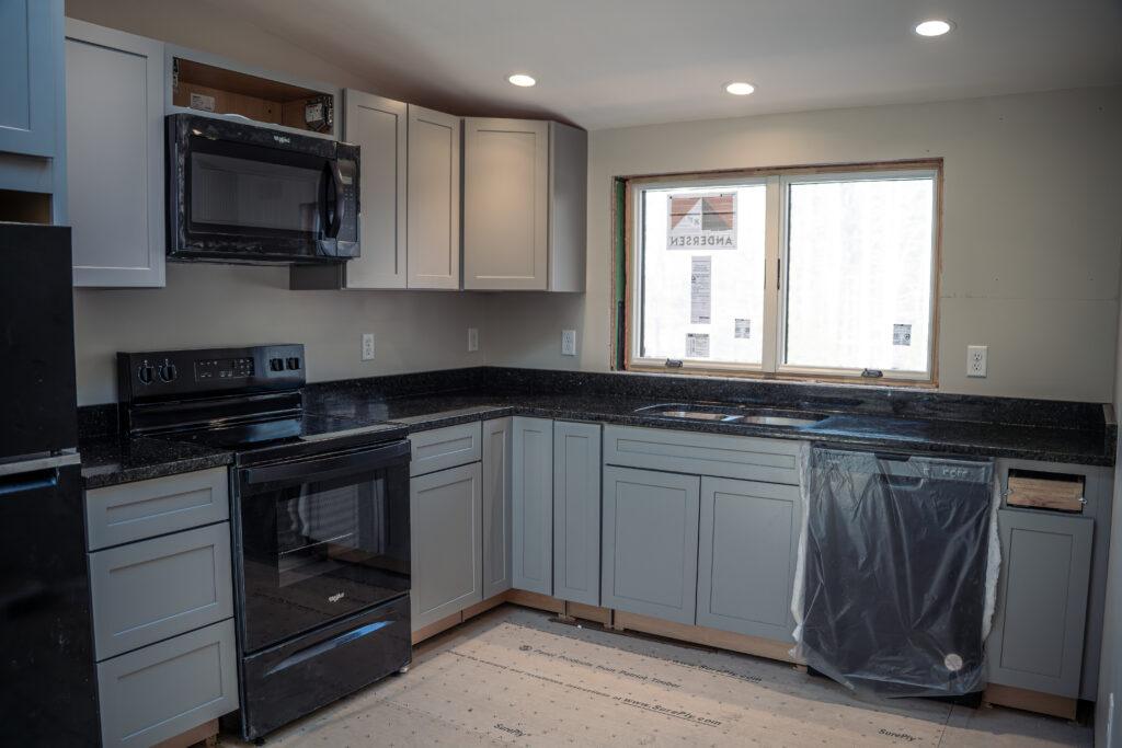 A new house with custom black kitchen countertops with grey cabinets. Black appliances are covered in protective clear plastic.