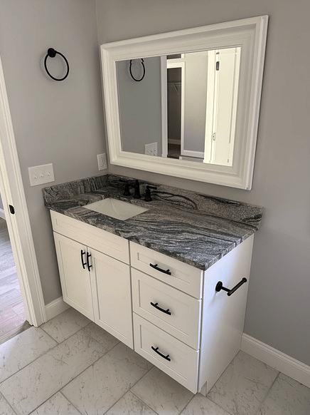 A bathroom vanity countertop with swirling shades of greys on white cabinets.