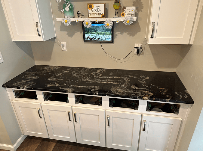 A gorgeous new black countertop with grey and gold swirls in it sitting on top of white cabinets.